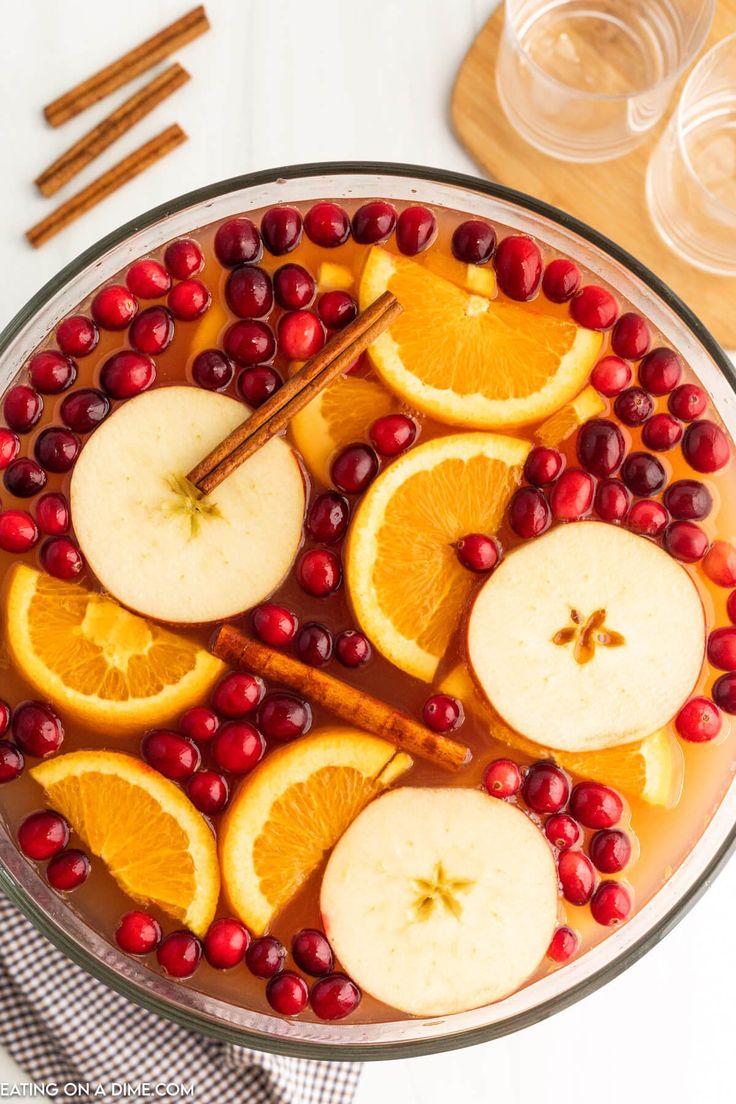 apples, oranges and cranberries are arranged in a bowl with cinnamon sticks