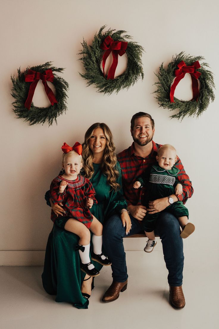 a family sitting on a bench in front of christmas wreaths with their baby and toddler