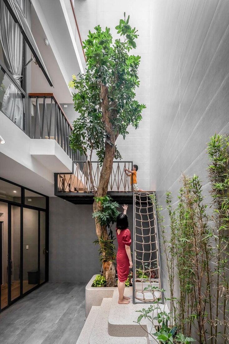 a woman in a red dress standing next to a tree and some stairs on the side of a building