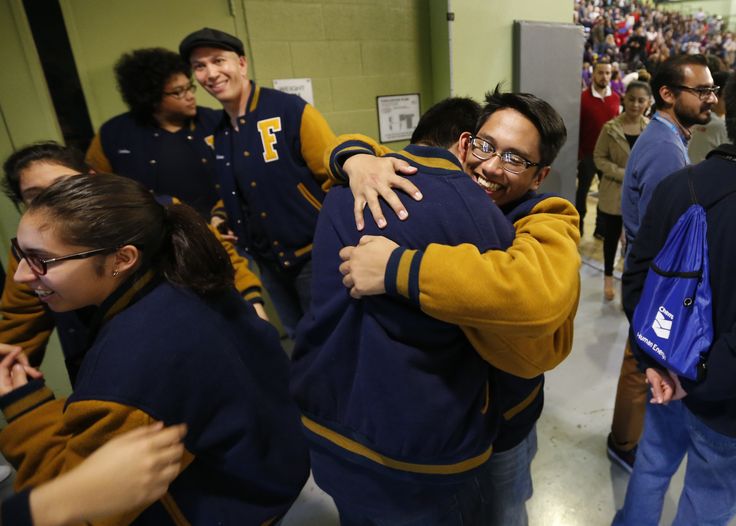 two men hugging each other in front of a group of people wearing blue and yellow jackets