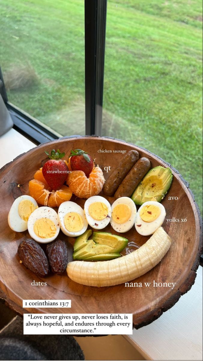 a wooden plate topped with different types of fruits and veggies next to a window