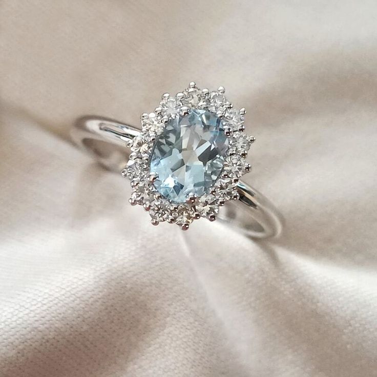 a ring with an aqua blue stone surrounded by white diamond halos on a light colored cloth