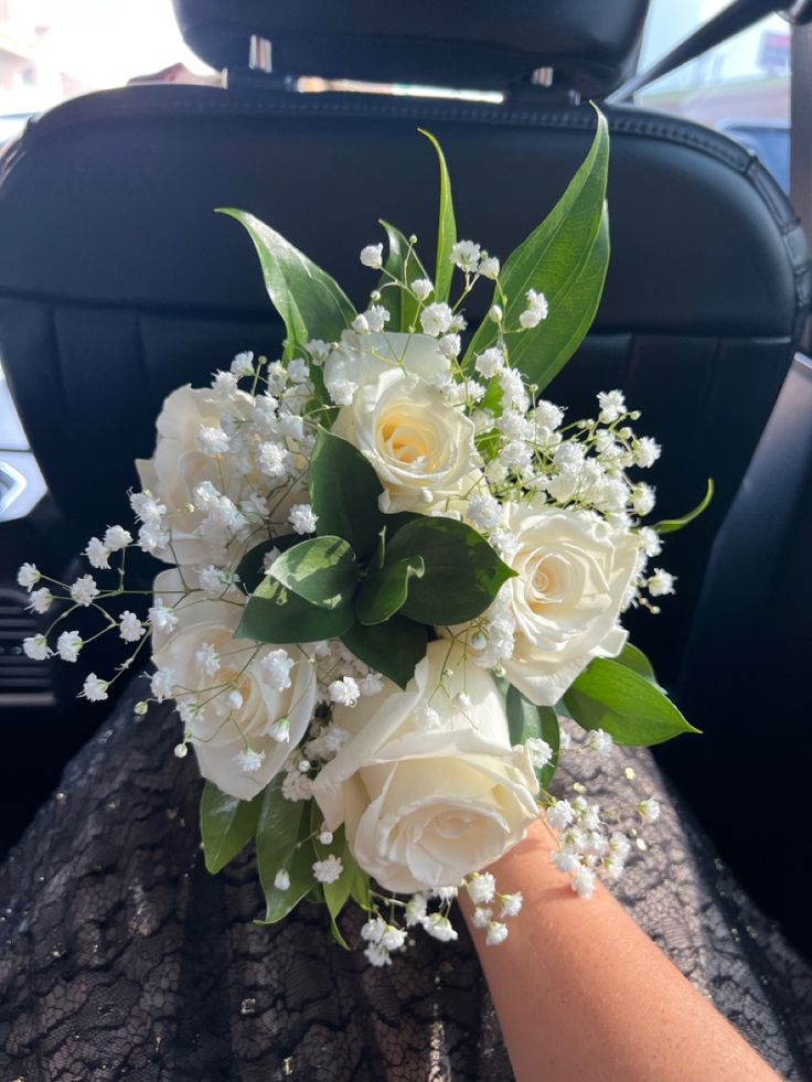 a bouquet of white roses and baby's breath sits on the back seat of a car