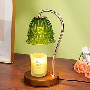 a green glass lamp sitting on top of a wooden table next to a vase with flowers