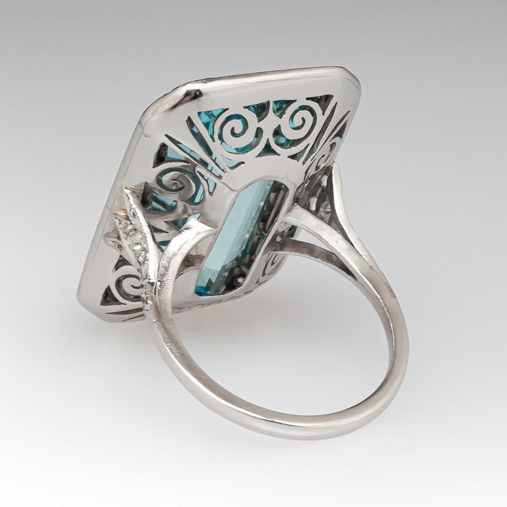 This mazing vintage cocktail ring is centered with one (1), bezel set, emerald cut natural aquamarine that is bordered with thirty-six (36), bead set, round single cut diamonds. The shoulders of the ring are each accented with three (3), bead set, round single cut diamonds. The gemstones are bordered with milgrain edging. The ring measures 28.9mm X 18.7mm at the top, rises 9.1mm above the finger, tapering to 1.7mm wide and 1.3mm thick at the base of the shank. It is currently a size 7. Art Deco Diamond Jewelry With Gemstone, Formal Multi-stone Rectangular Ring, Blue Topaz Emerald Cut Ring With Bezel Setting, Emerald Cut Blue Topaz Ring With Bezel Setting, Elegant Multi-stone Rectangular Rings, Rectangular Emerald Ring With Accent Stones For Formal Events, Rectangular Emerald Ring With Accent Stones For Formal Occasions, Silver Emerald-cut Topaz Ring With Gemstone Accents, Rectangular Emerald Jewelry With Bezel Setting