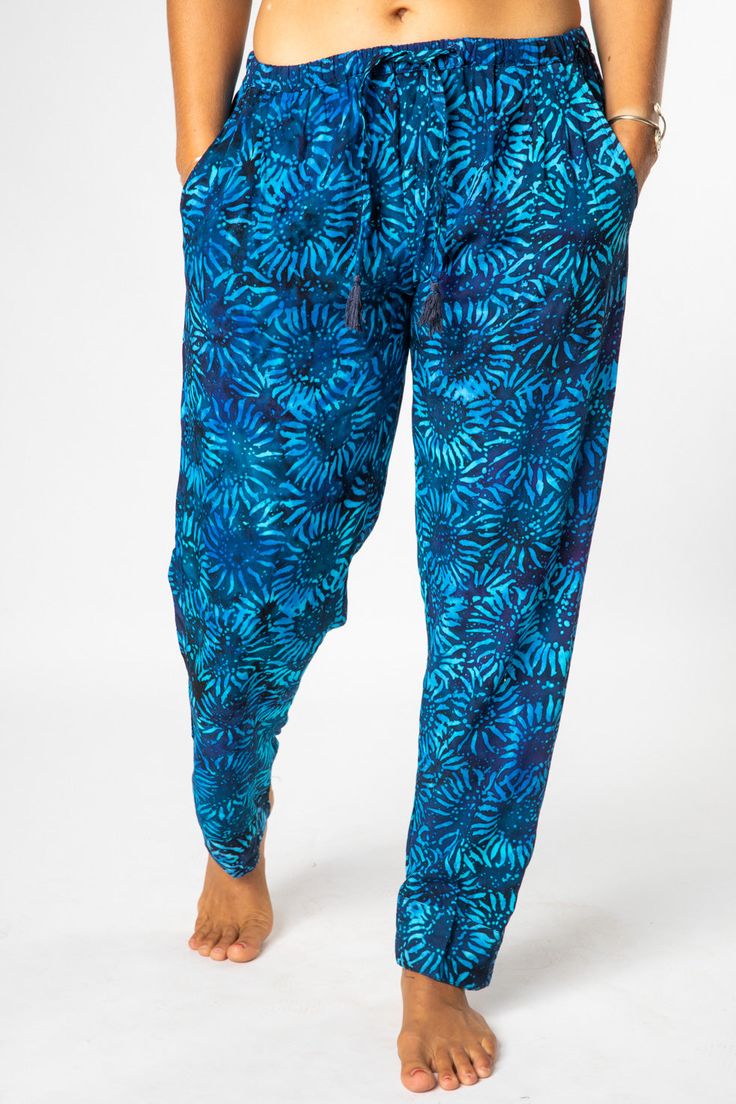 A combination of cool comfort and colorful hippie style are all yours when you slip into these breezy batik straight legged lounge pants. Featuring flowing rayon fabric and an elasticized waist with a drawstring for a cozy and comfortable fit. Each pair of drawstring comfy pants was hand dyed and ethically made by our makers in Bali. The traditional Indonesian batik dye process is an ancient artform and each pair of one of a kind pants helps support this ancient artistic tradition. The perfect p Bohemian Rayon Harem Pants For Vacation, Casual Multicolor Harem Pants For Beach, Blue Relaxed Fit Harem Pants For Vacation, Blue Harem Pants For Vacation, Tropical Loungewear Pants, Bohemian Blue Rayon Bottoms, Bohemian Rayon Harem Pants For Beach, Bohemian Lounge Pants With Elastic Waistband, Blue Relaxed Fit Harem Pants For Beach