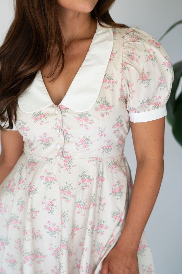 Expertly designed Claire Collar Mini Dress boasts a pink and green floral print, contrasting with a crisp white collar and quarter pearl button closures along the front. Short puff sleeves and a white waist tie add feminine charm, while a side zipper closure ensures a secure fit! 100% rayon, lined Model is 5'3" with a 32" bust, 25" waist, and 38" hips and wearing a small. Size recs: 0-2:S, 4-6:M, 8:L Fitted Floral Print Dress With Collar, Spring Collared Feminine Mini Dress, White Collared Dress For Garden Party, White Collared Dress For Spring, Feminine Summer Mini Dress With Lace Collar, Spring Floral Print Dress With Collared Neckline, Spring Cream Dress With Peter Pan Collar, Pink Peter Pan Collar Dress For Spring, Pink Spring Dress With Peter Pan Collar