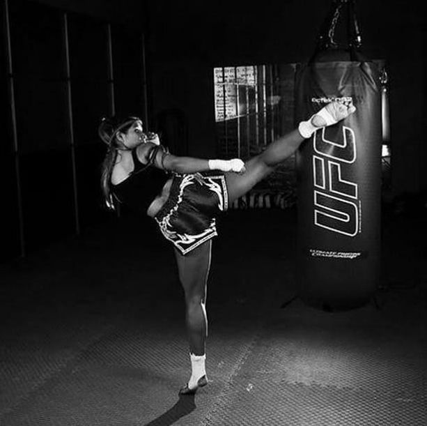 a woman kicking a kick with her leg in the air while standing next to a punching bag