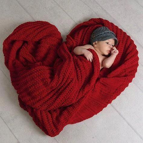 a baby wrapped in a red blanket is laying on the floor with his head resting on his hand