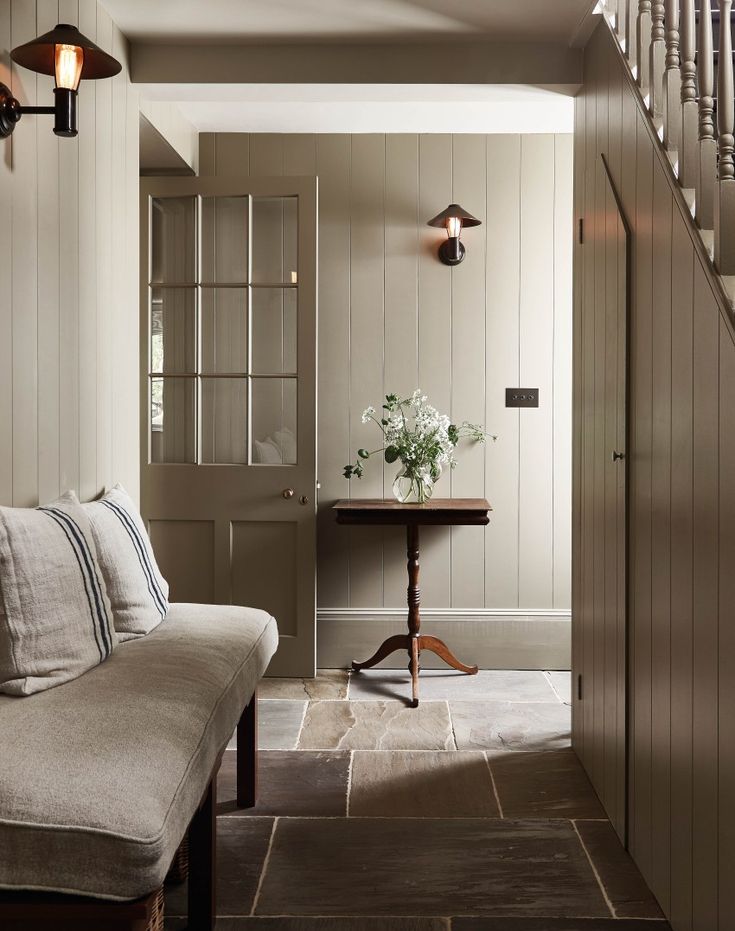 a living room filled with furniture next to a wooden stair case and wall mounted sconces