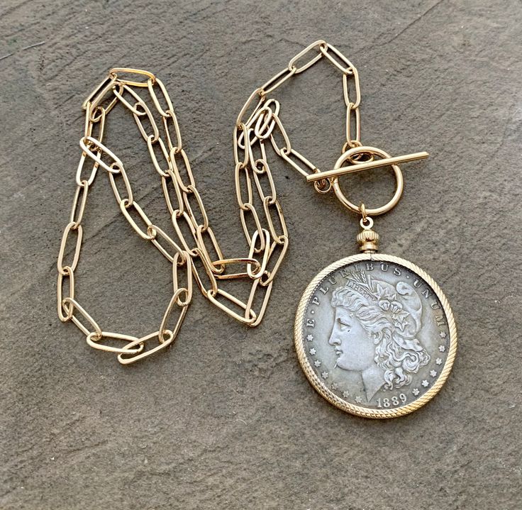 December 4th will be the last day to order for Christmas delivery. Please review the production and estimated delivery timeframe for this listing before purchasing - thank you .A beautiful replica antique American silver dollar 1889 coin cast in silver pewter is encircled in a gold palted brass coin holder with an 8mm brass ring bail. It hangs from a gold paperclip style chain with a front closure oversized toggle clasp. Also available with a back closure in a lobster claw clasp. The coin with b Antique Coin Necklace, Gold Coin Jewelry, 25 Anniversary, Mixed Metal Necklace, December 4th, Custom Coins, Rustic Glam, Antique Coins, Coin Pendant Necklace