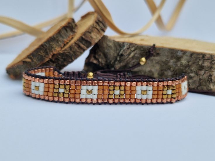 a beaded bracelet sitting on top of a piece of wood next to a tree