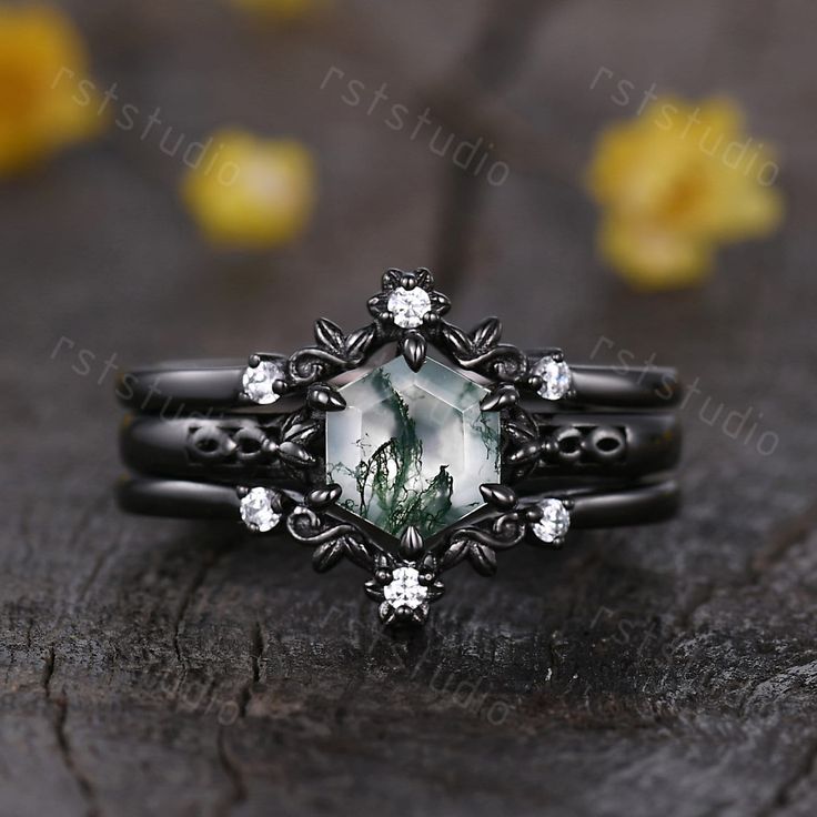 a black ring with a green stone surrounded by white diamonds on a piece of wood