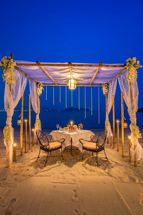 an outdoor dining area on the beach at night with candles lit up in front of it