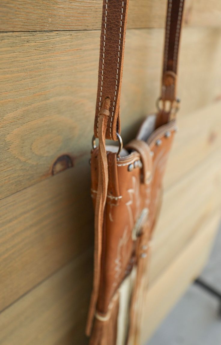 Fort Benton Boot Crossbody Bag Looking for something unique ... well here it is! The Fort Benton Boot Crossbody Bag is handcrafted in Texas, U.S.A. This one of a kind leather bag is made from recycled cowboy boots! Features cream stitched brown leather uppers adorned with buckle and leather accent, leather strap with magnetic closure, leather horse reins as strap, and brown and cream hand stitched leather fringe. This Western bag is the perfect size to hold your phone, small wallet, and a few es Hand Tooled Leather Bags For Rodeo, Western-themed Brown Leather Shoulder Bag, Western Style Hand Tooled Brown Shoulder Bag, Western Style Brown Hand Tooled Shoulder Bag, Brown Leather Bags For Rodeo, Leather Hand Tooled Shoulder Bag For Western-themed Events, Hand Tooled Brown Bags For Rodeo, Brown Hand Tooled Bag For Rodeo, Hand Tooled Brown Bag For Rodeo