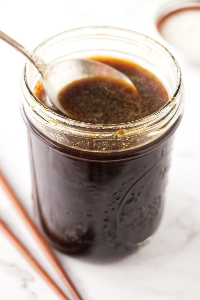 two spoons in a jar filled with brown liquid next to chopsticks on a white surface