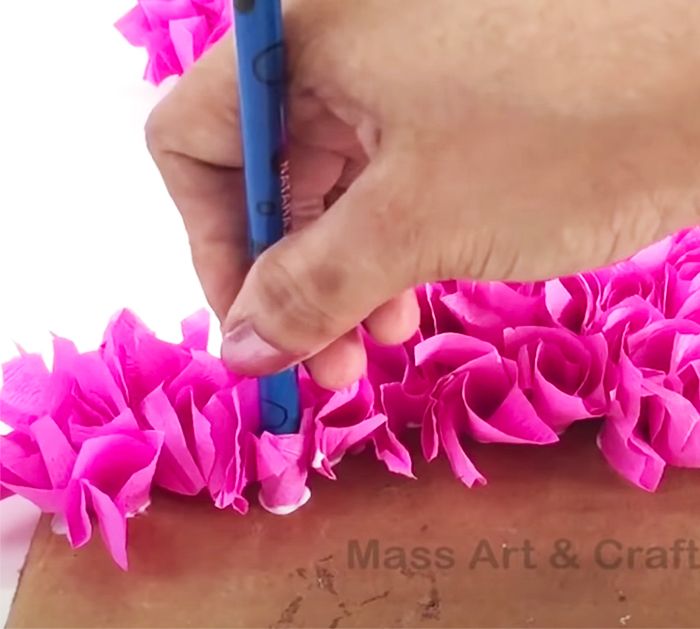 a person using a blue pen to cut pink paper flowers on a piece of cardboard