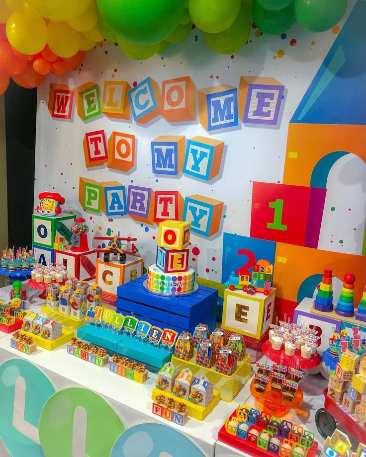 a birthday party with colorful decorations and balloons on the wall, including blocks that spell out welcome to my baby