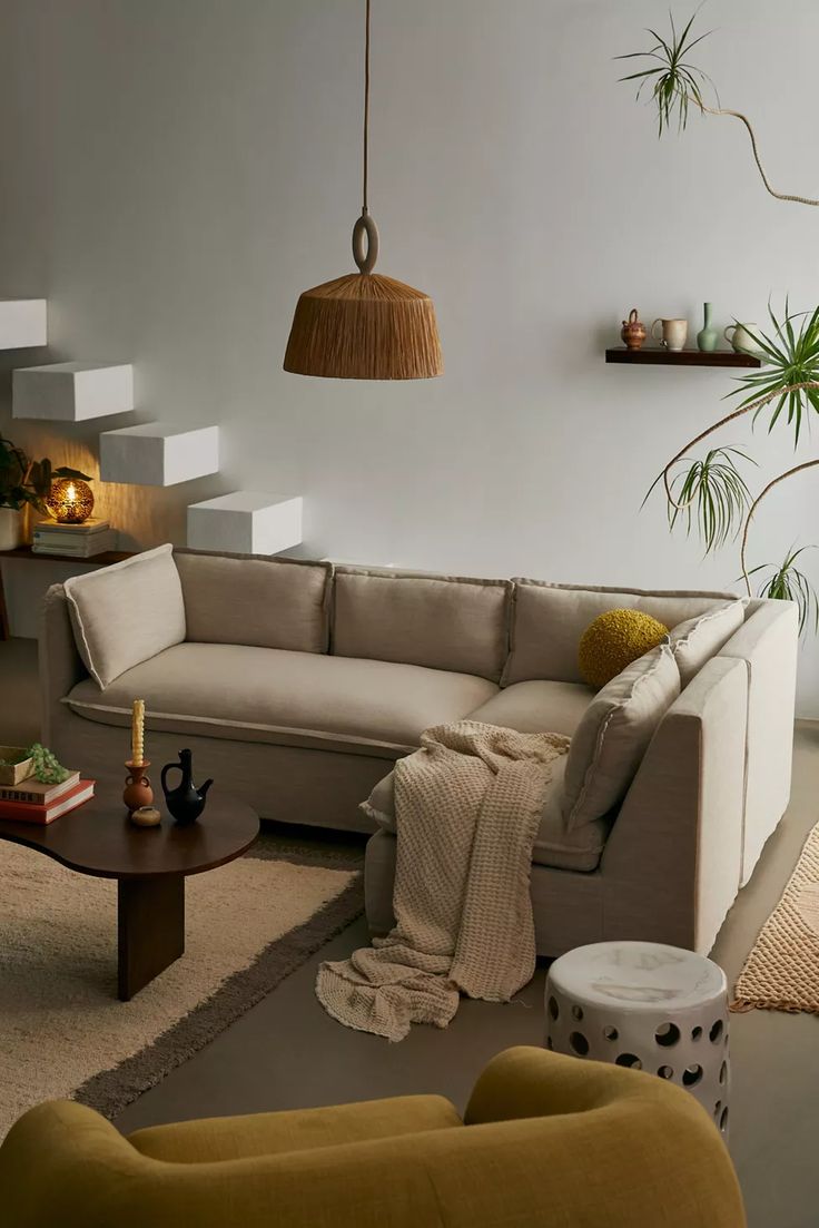 a living room filled with furniture next to a stair case and potted plant on the wall