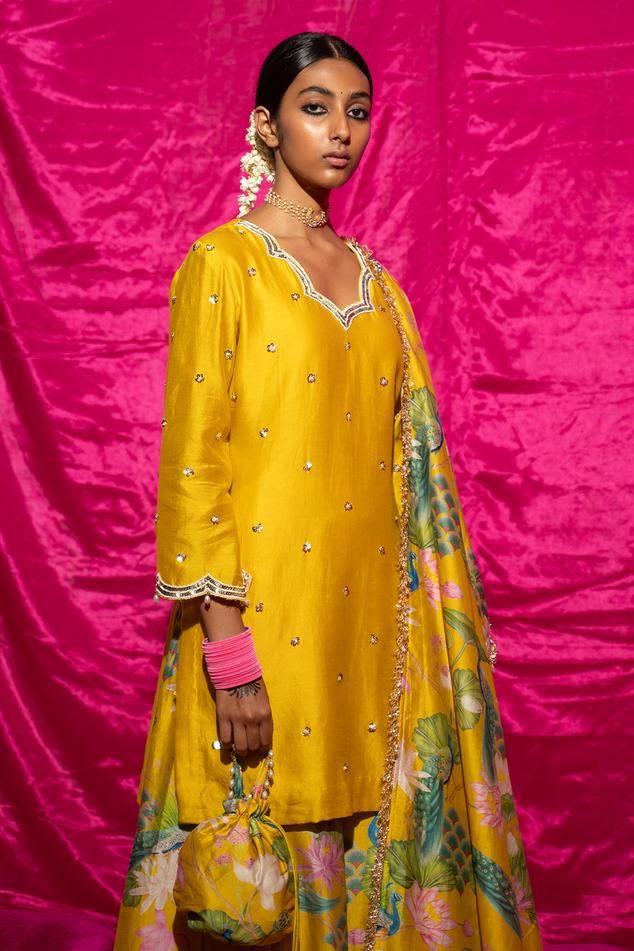 Yellow chanderi silk kurta with sequin, pearl placement embroidery. Paired with floral print sharara and fringe bordered dupatta.
Components: 3
Pattern: Printed, Embroidery
Type Of Work: Floral, sequin, pearl
Neckline: Scallop V neck
Sleeve Type: Long sleeves
Fabric: Chanderi Silk, Lining: Shantoon
Color: Yellow
Other Details: 
Fringe tassel bordered dupatta
Length:
Kurta: 35 inches
Sharara: 38 inches
Note: Potli shown in the image is not for sale
Occasion: Sangeet - Aza Fashions Designer Festive Sharara With Gota Work, Designer Wear Sharara With Gota Work For Festive Season, Chanderi Sets With Gota Work For Eid, Festive Sharara With Mirror Work, Designer Chanderi Sharara With Resham Embroidery, Festive Chanderi Palazzo Set With Mirror Work, Dola Silk Palazzo Set With Mirror Work, Silk Palazzo Set With Mirror Work And Straight Kurta, Bollywood Silk Set With Zari Work