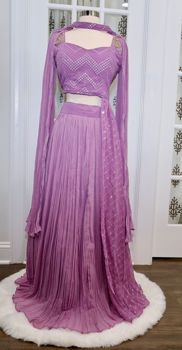 Beautiful Lavendar Crop top/Lehanga set with attached Trail on one side of the Blouse. The dress has elegant Zig zag pattern lucknawi work on Top and zardosi work on the shoulder. Sleeves are also provided. Comes with Butterfly style Dupatta with sequin work on it. Color: Lavender Size: XL 42 plus 2 inchesFabric: GeorgetteLehanga Waist: 39 inchesLehanga Length: 40 and 1/2 Inches Embellishments: Lucknawi work with sequin, mirror and zardosi work on top. Note: We accommodate on size adjustments wh Navratri Purple Palazzo Set With Cutdana, Purple Georgette Palazzo Set With Traditional Drape, Traditional Drape Purple Georgette Palazzo Set, Diwali Purple Palazzo Set With Traditional Drape, Purple Palazzo Set With Pallu For Navratri, Traditional Sets With Dupatta And Side Open, Bollywood Style Purple Palazzo Set With Mirror Work, Traditional Side Open Sets With Dupatta, Bollywood Style Designer Purple Palazzo Set