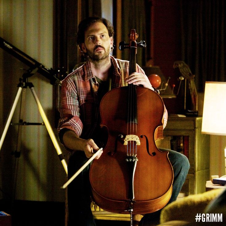 a man sitting in front of a cello on top of a wooden floor next to a lamp