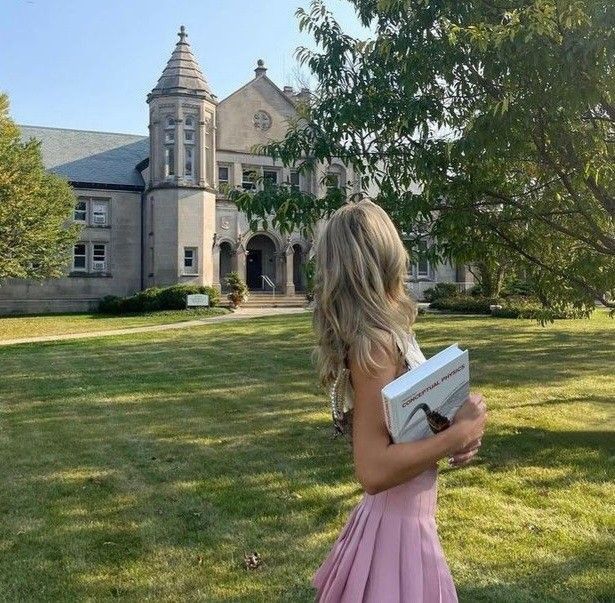 a girl in a pink dress is holding a book and looking at the building behind her