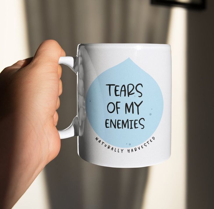 a person holding a coffee mug with the words tears of my enemies on it