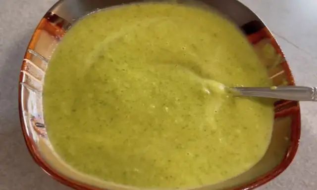 a red bowl filled with green soup on top of a counter next to a silver spoon