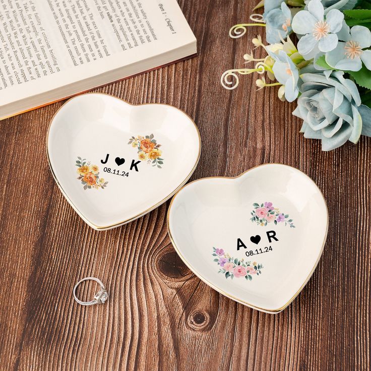 two heart shaped dishes with initials and flowers on them, next to an open book