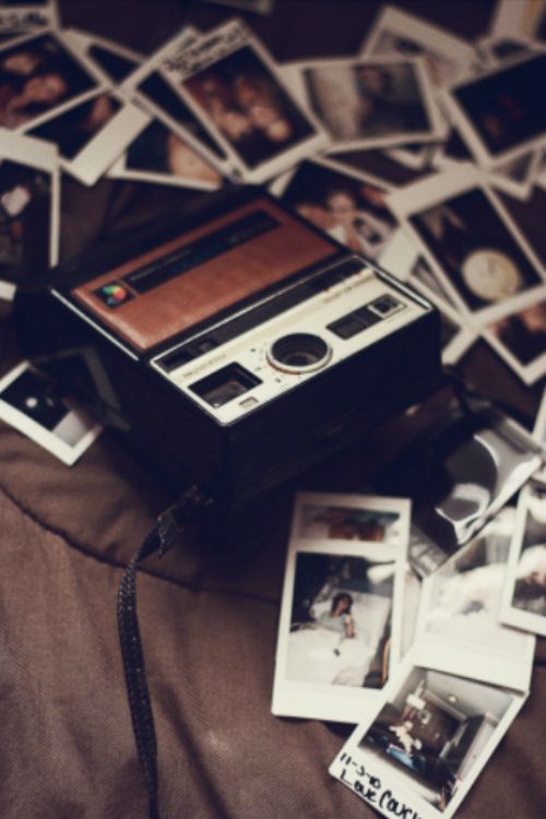 an old camera sitting on top of a bed covered in polaroid pictures and photos