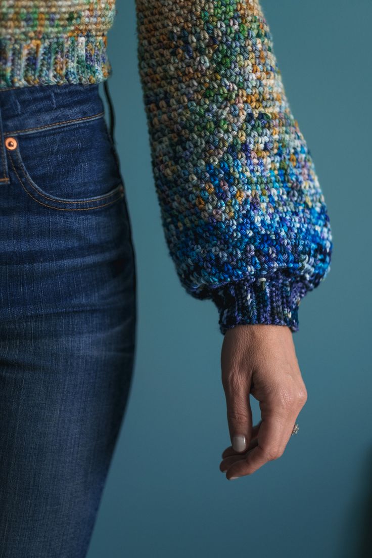 a close up of a person's hand holding something in their left hand and wearing a colorful knitted sweater