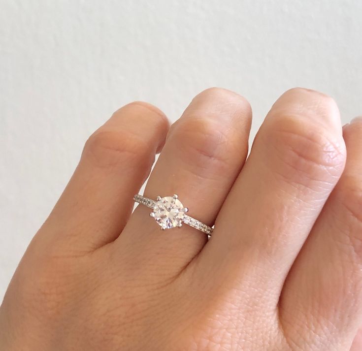 a woman's hand with a diamond ring on top of her finger, showing the side view