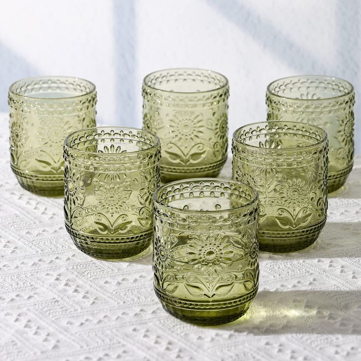 six green glass cups sitting on top of a white doily tablecloth with lace