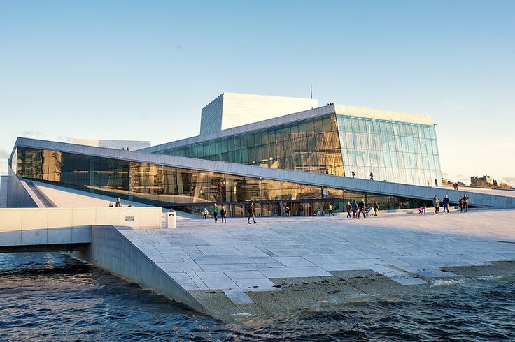 people are walking around in front of a large building on the water's edge