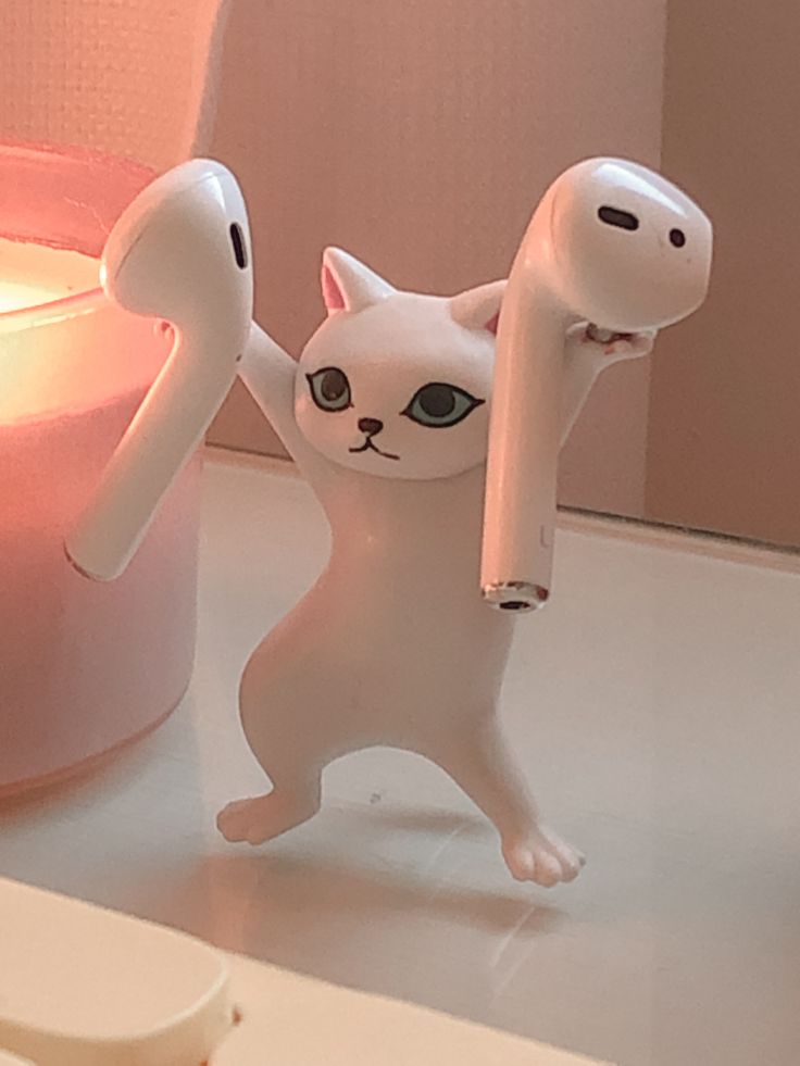 a white cat figurine holding a pink object in front of a lit candle