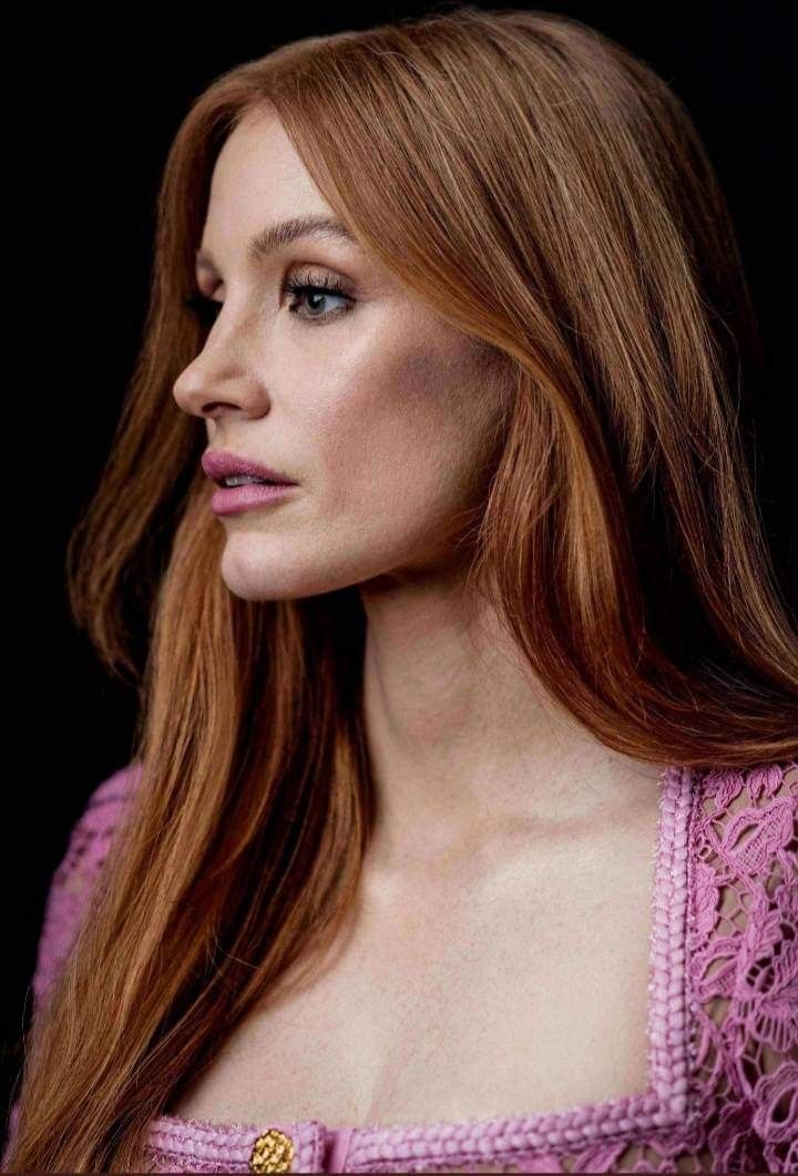 a woman with long red hair wearing a pink dress and gold brooch on her left shoulder