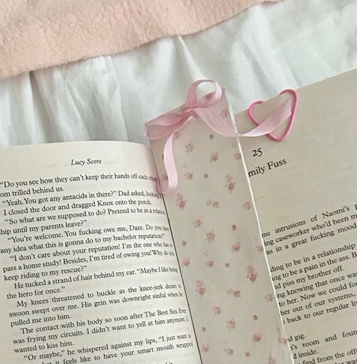 an open book with a pink ribbon tied around it's neck and the pages are folded in half