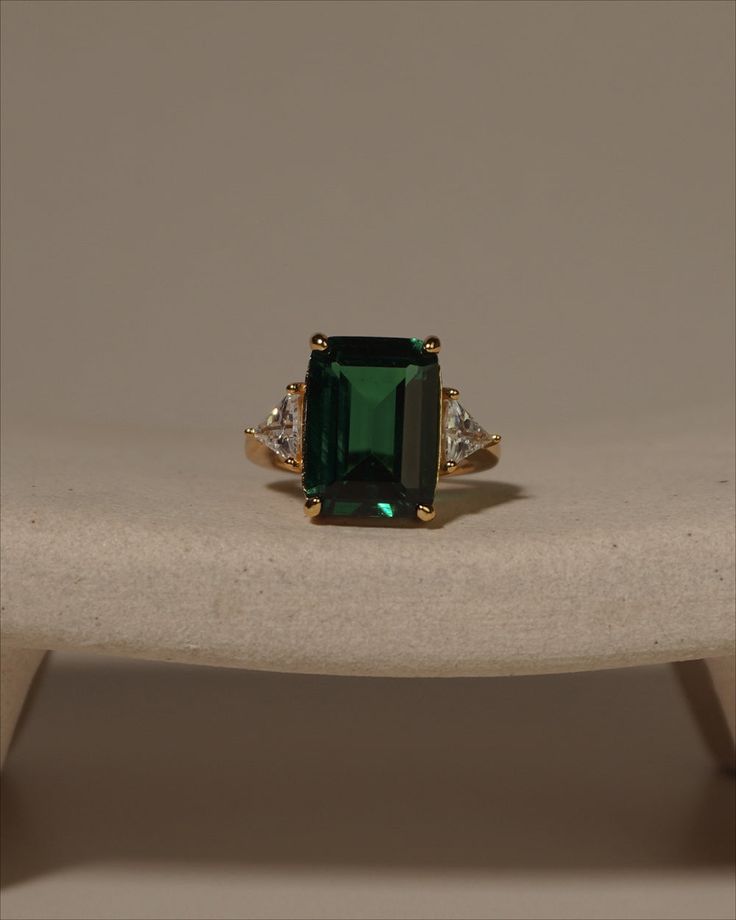 an emerald and diamond ring sitting on top of a table