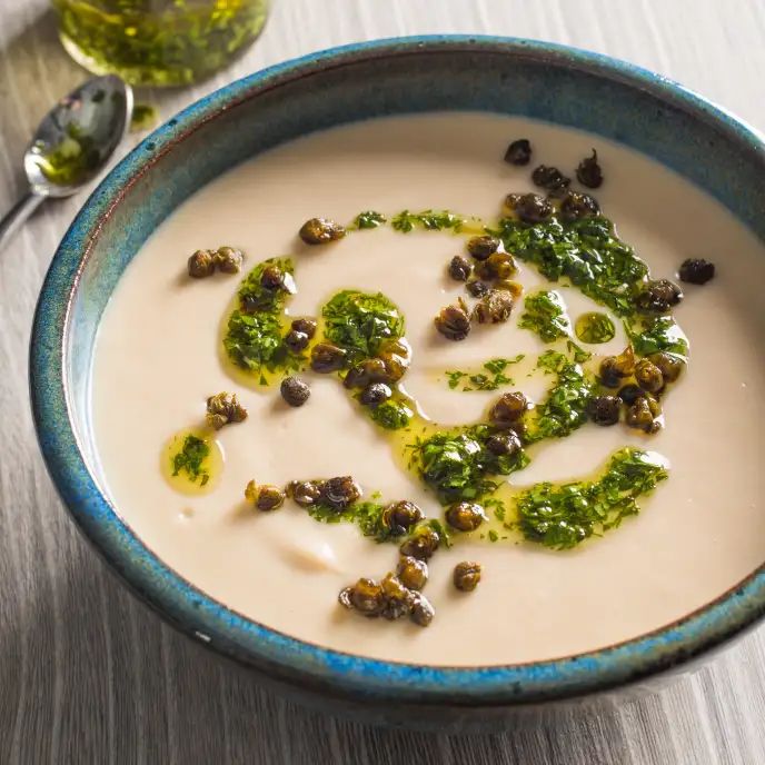 a blue bowl filled with soup and garnished with green toppings next to a spoon