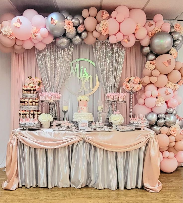 a table topped with lots of pink and silver balloons next to a wall filled with cake