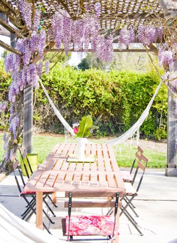 a wooden table sitting under a purple wister covered pergola arbor with hammocks hanging from it