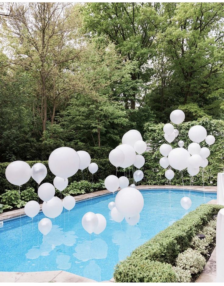 white balloons floating in the air over a pool