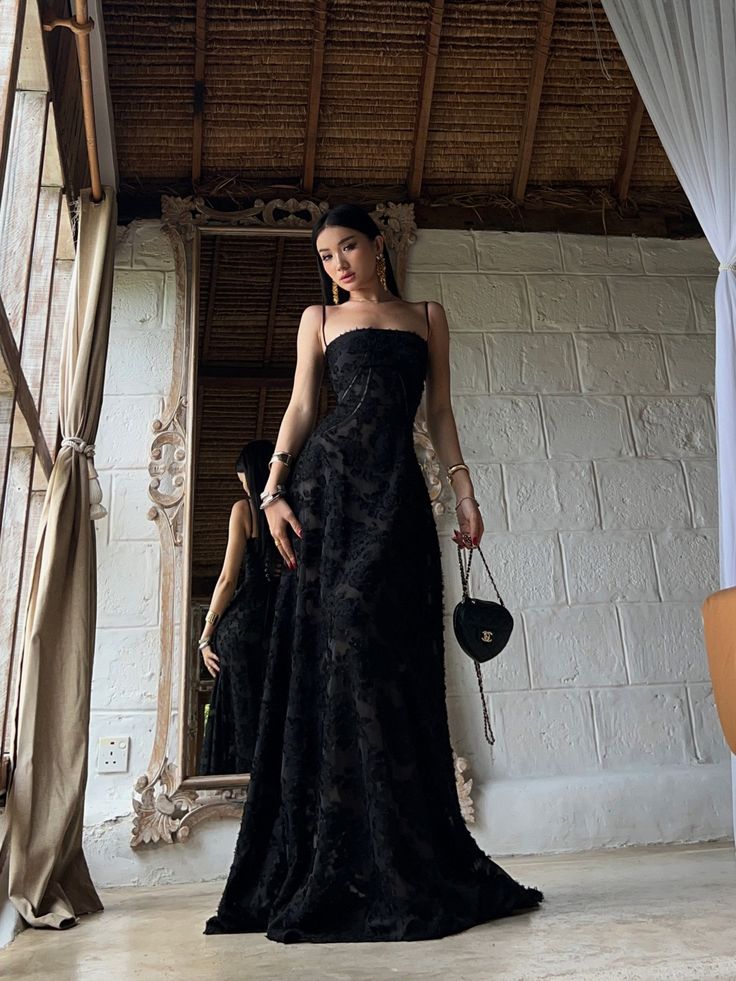 a woman standing in front of a mirror wearing a black dress and holding a purse