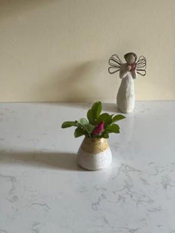 two small vases with flowers in them sitting on a white counter top next to an angel figurine