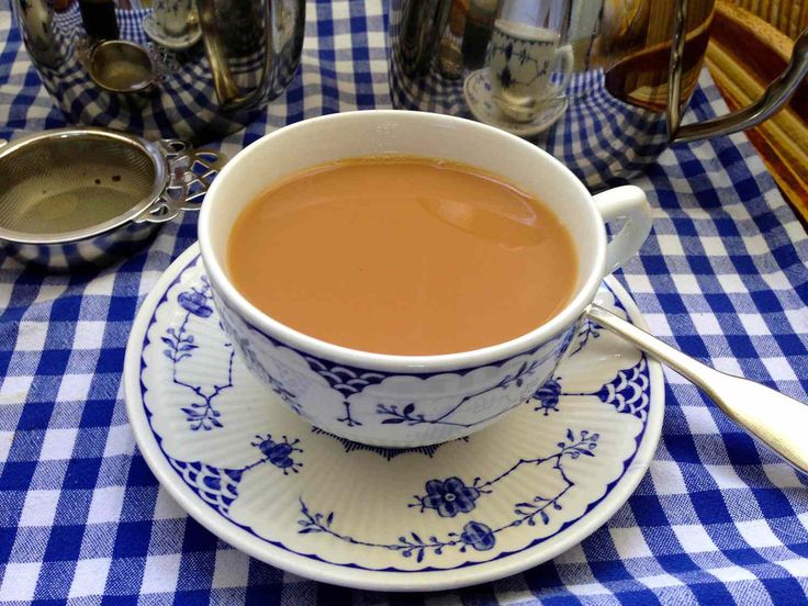 a cup of tea sits on a blue and white checkered tablecloth with spoons