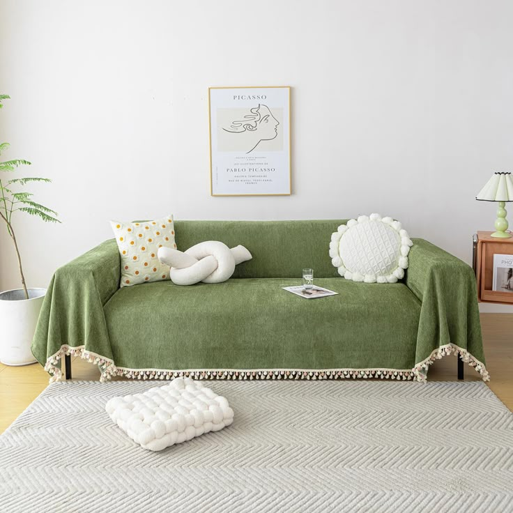 a living room with a green couch covered in a blanket and two pillows on the floor