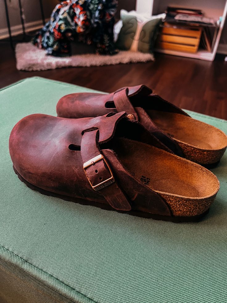 Pair of brown leather clog shoes by Birkenstock. Cork footing. Resting on a light green ottoman.