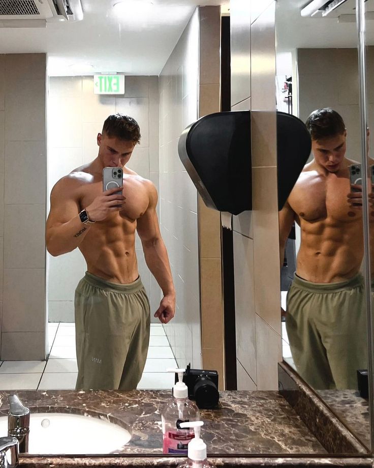 a shirtless man taking a selfie in front of a mirror with his cell phone