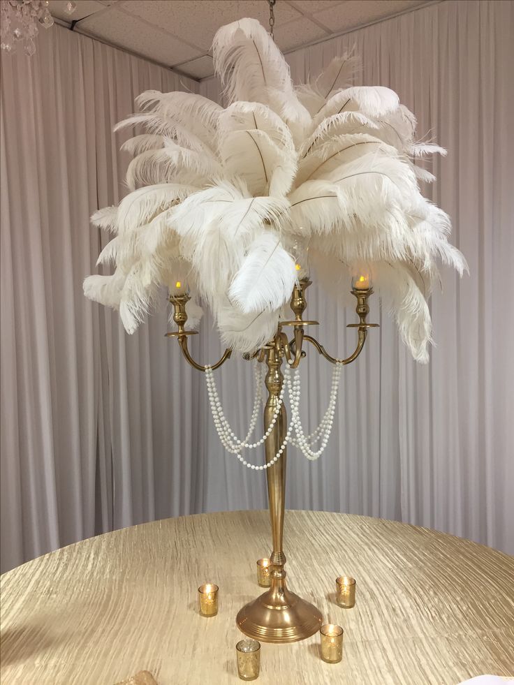 a table topped with a gold candelabra covered in white feathers and beads